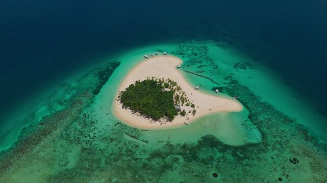 High altitude aerial backward flight with gimbal tilt up over Patawan Island, Balabac, Philippines. Reverse tracking drone shot reveals tropical reef and ocean horizon.