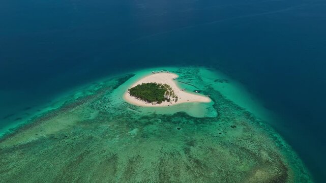 Long distance high altitude aerial tracking orbit of Patawan Island moving left to right, Balabac, Philippines. Clockwise drone shot showcases isolated tropical island and turquoise reef.