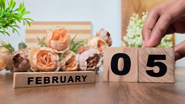 Hand placing wooden calendar blocks showing february 5 on a wooden table