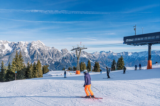 Skiers enjoy a sunny day on the groomed slopes near the modern ski lift station in Saalbach, Austria. The majestic snowy Alps provide a stunning backdrop for winter sports.