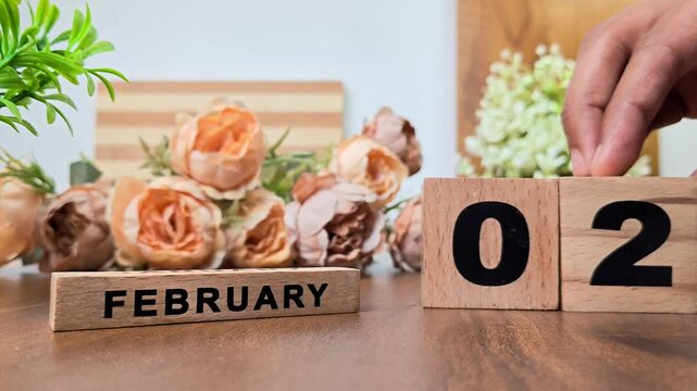 Hand placing wooden calendar blocks showing february 2 on a wooden table