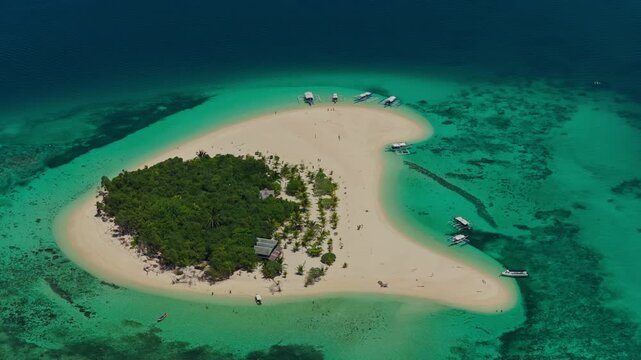 High altitude aerial tracking orbit of Patawan Island moving left to right, Balabac, Philippines. Clockwise panoramic drone shot showcases tropical island, white sand beach, and turquoise coral reef.