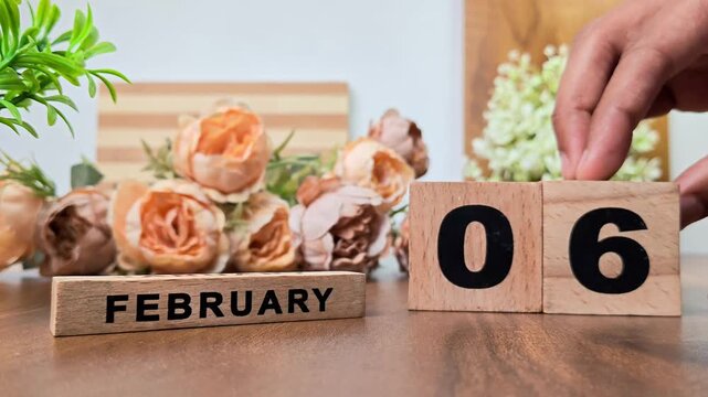 Hand placing wooden calendar blocks showing february 6 on a wooden table