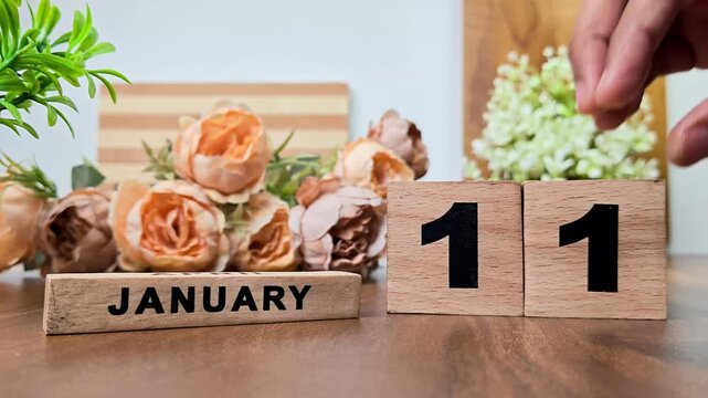 Hand placing wooden calendar blocks showing january 11 on a wooden table