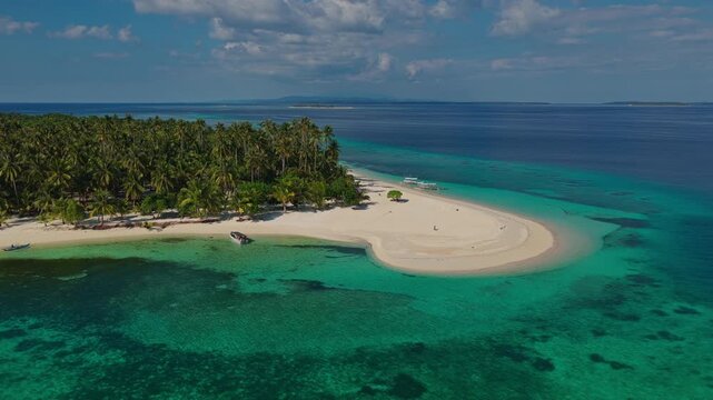 Medium range aerial tracking orbit of Tangkahan Island moving left to right, Balabac, Philippines. Clockwise drone shot reveals tropical hook sandbar and clear reef waters.