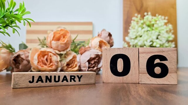 Hand placing wooden calendar blocks showing january 6 on a wooden table