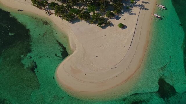 Aerial vertical descent facing the hook-shaped sandbar of Tangkahan Island, Balabac, Palawan, Philippines. Drone drops down smoothly over tropical reef and crystal clear turquoise sea.