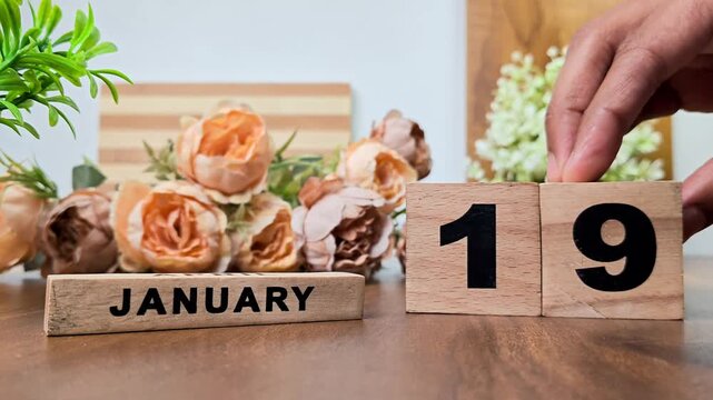 Hand placing wooden calendar blocks showing january 19 on a wooden table