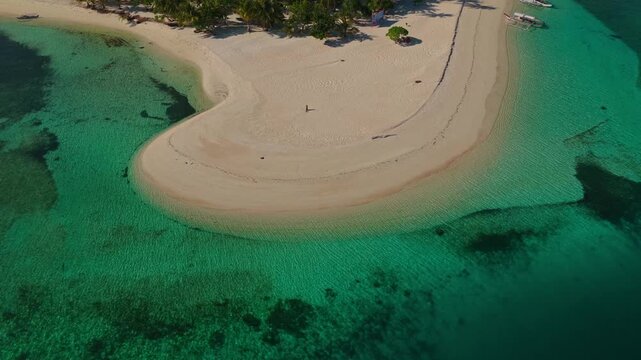 Aerial vertical descent with gimbal tilt up over Tangkahan Island, Balabac, Palawan, Philippines. Drone drops down over turquoise reef while tilting up to reveal tropical hook sandbar.