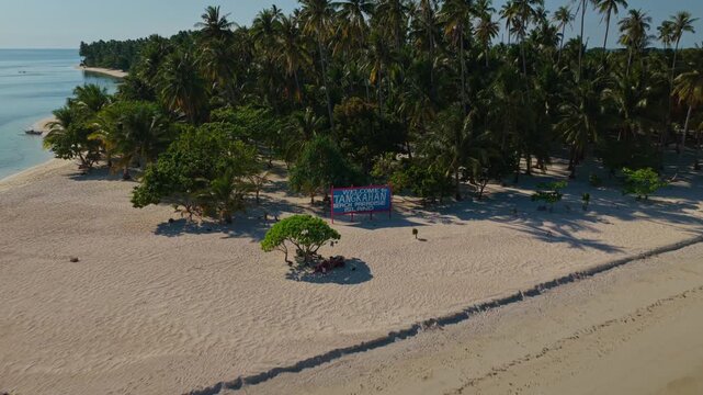 Aerial backward reveal flight of Tangkahan Island, Balabac, Palawan, Philippines. Pull away drone tracking shot showcases tropical palm trees, a unique hook-shaped white sandbar, and turquoise ocean.