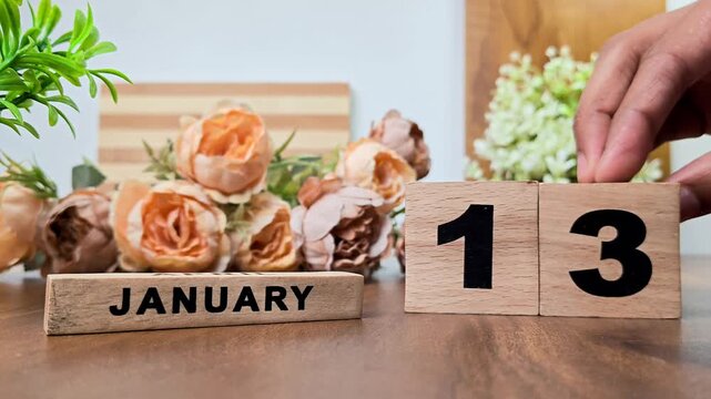 Hand placing wooden calendar blocks showing january 13 on a wooden table
