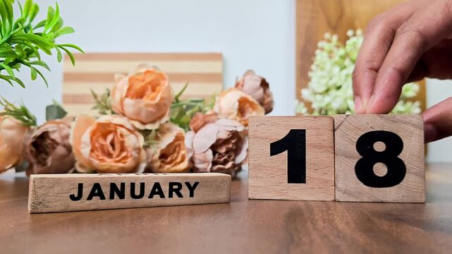 Hand placing wooden calendar blocks showing january 18 on a wooden table