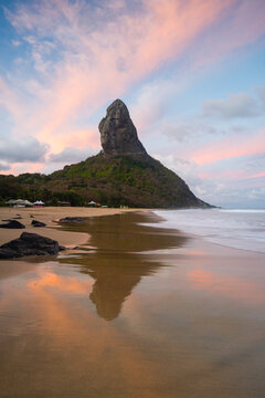 Morro do Pico with a pink sky reflected on the wet sand, Fernando de Noronha, Pernambuco, Brazil