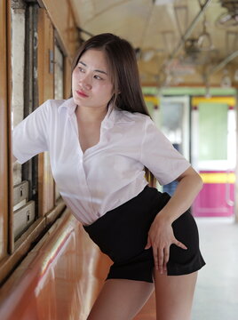 A young Asian woman in a white student uniform shirt and black skirt poses inside an old train car