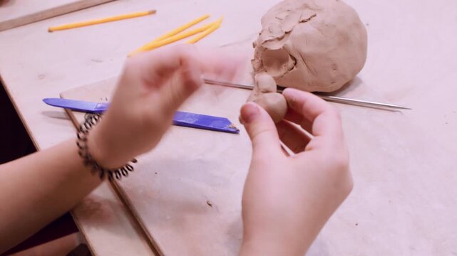 Kids craft. Creative learning. Unrecognizable child hands shaping ceramic molding raw using color tool in professional artisan studio.