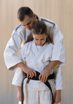 Martial arts instructor helping young girl tie black belt during training