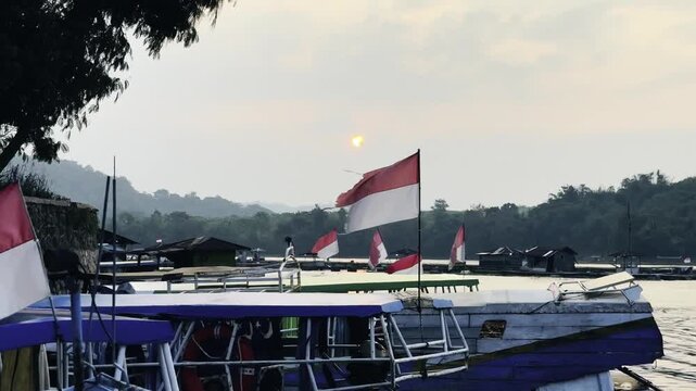 A static b-roll shot of several Indonesian red and white flags waving gently from the roofs of traditional wooden tourist boats.