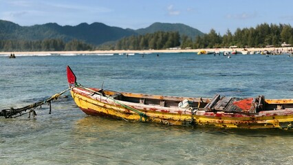 Rustic wooden boat anchored in clear turquoise water by a tropical beach with lush green mountains under blue sky © suciramadhani