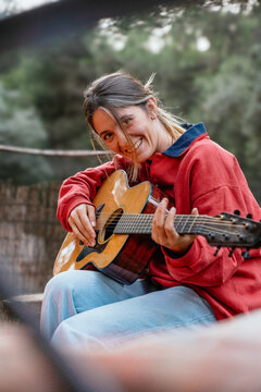 Woman laughing playing acoustic guitar outdoors