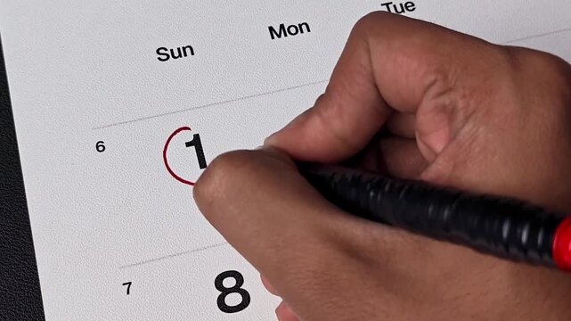 Hand circling number 1 on a monthly calendar planner