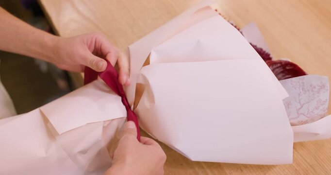 Bouquet presentation. Flowers packaging. Professional female florist hands tying ribbon preparing chrysanthemum in workshop.