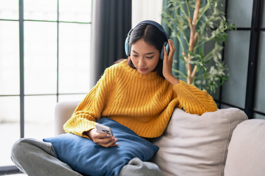 Asian girl in yellow sweater wear headphone listen to music on smartphone