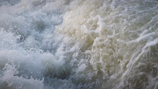 Spring meltwater cascades over Sauble Falls in Ontario. The slow motion framing reveals individual water droplets suspended in mid-air above the churning, frothy rapids.