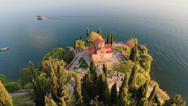 Drone flies above treetops toward Church of St. John at Kaneo above Lake Ohrid.