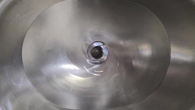 Water draining and swirling in a stainless steel sink until it completely drains.