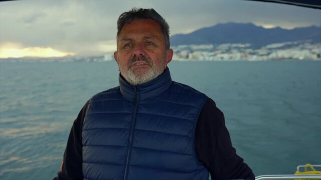 man standing still by ocean with mountains in the background, neutral expression, blue jacket, travel adventure, natural light, clean background, copy space, modern design, resource for web.