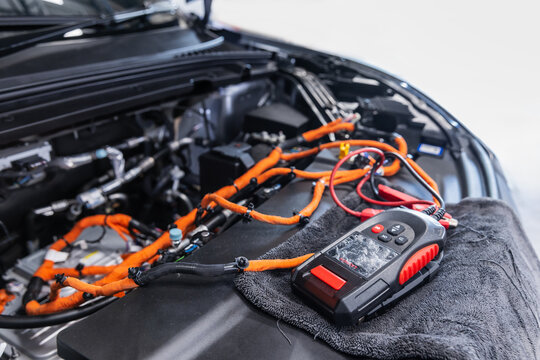 Professional diagnostic scanner positioned beside the high-voltage electrical system of an electric vehicle during maintenance inspection.