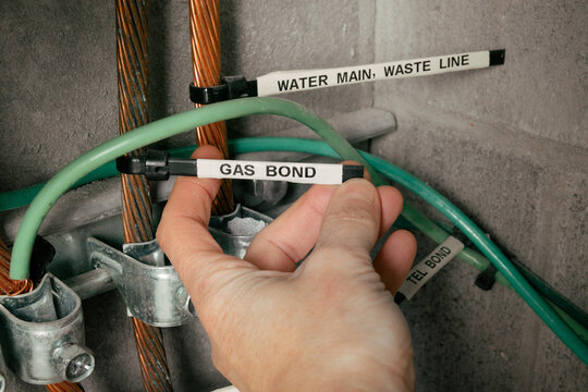 Gas bond label on grounding rod, electrical room busbar system. Electrician inspecting grounding rod labels. Copper conductors and clamps mounted on wall in electrical room. Selective focus.