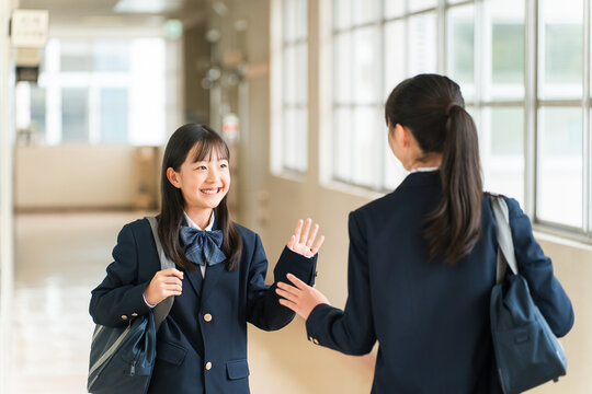 Elementary, middle, and high school girls in uniform walking down a school corridor.