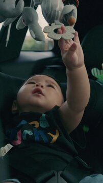 Cute Toddler Reaching for Hanging Toys While Sitting in Child Safety Car Seat, Family Travel Concept in 4K	