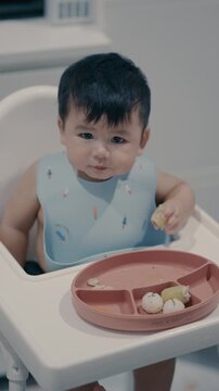 Adorable little baby toddler practicing baby-led weaning BLW at home with green bokeh background.