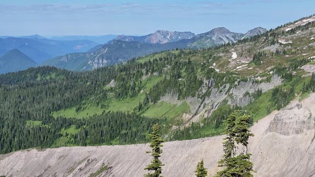 Panning view of mountain range with pine trees and snow patches