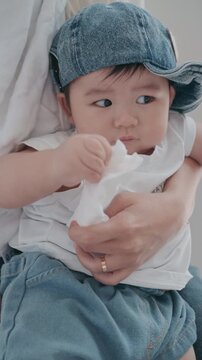 4K Vertical close up of a cute Asian baby boy wearing a denim hat in his mother's arms.