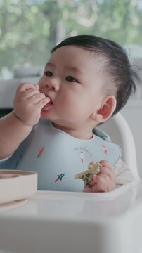 Adorable little baby toddler practicing baby-led weaning BLW at home with green bokeh background.