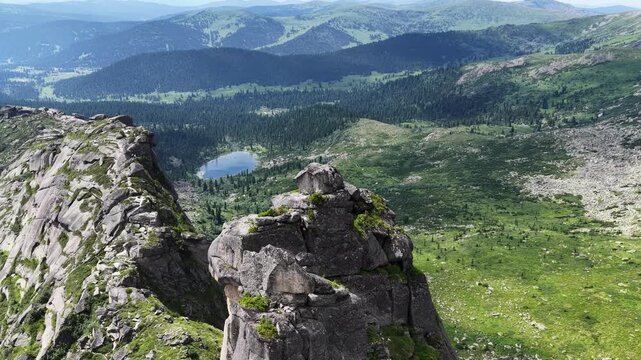  Breathtaking aerial view of a pristine mountain lake surrounded by sharp rocky peaks and dense green pine forest on a bright summer day.