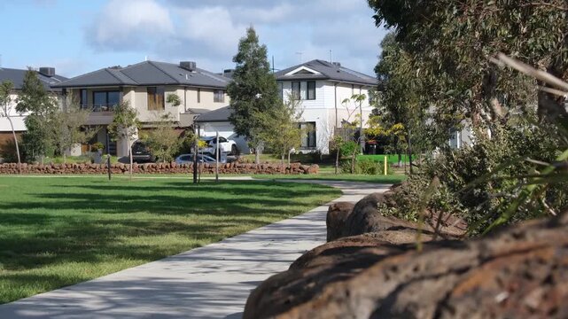 Modern two-story houses or contemporary family homes facing a green public park and footpath in a new residential estate, Melbourne outer suburbs, Victoria, Australia.