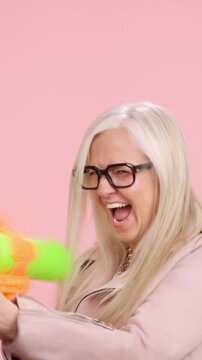 Playful senior woman shooting a water gun