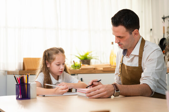 Father helping daughter with homework in the kitchen, Dad and little daughter studying and drawing together at home, Caring father teaching young daughter to do schoolwork