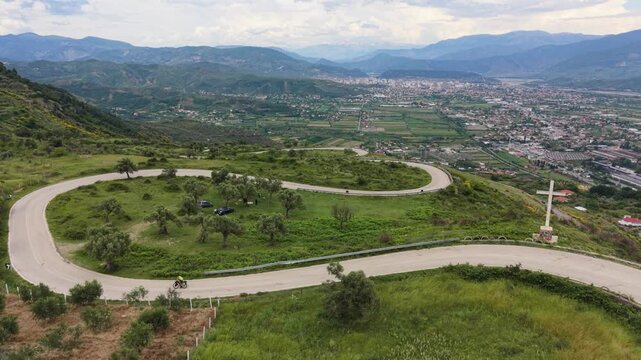 Slow drone flight follows a cyclist on a winding road near Elbasan, Albania.