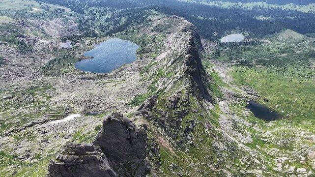 Breathtaking aerial view of a pristine mountain lake surrounded by sharp rocky peaks and dense green pine forest on a bright summer day.