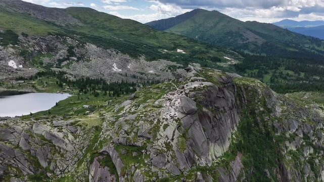 High angle drone shot of majestic mountain ridges and alpine lake hidden in deep coniferous woodland during sunny summer season.
