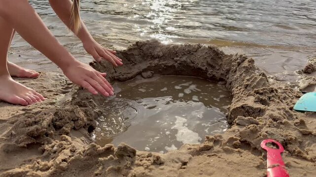 children digging a water-filled hole in the sand with plastic shovels. Enjoying a classic summer activity by the water's edge.