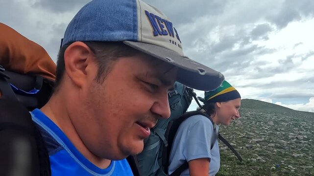 Hikers trekking close-up side view in Georgia, carrying backpacks and using poles on mountain route for Caucasus tourism, expedition planning, endurance training, and outdoor adventure footage