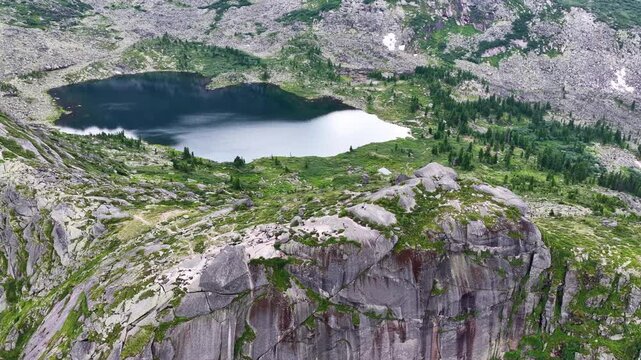  Breathtaking aerial view of a pristine mountain lake surrounded by sharp rocky peaks and dense green pine forest on a bright summer day.
