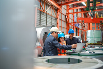 Fototapeta premium Factory supervisor leading production review with engineering team using laptop inside steel warehouse. Industrial planning, inventory control, manufacturing efficiency and workplace collaboration.