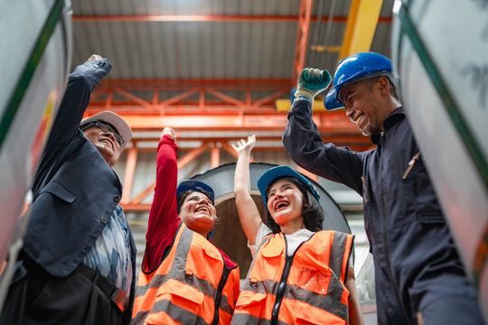 Engineering team cheering after completing production target inside steel warehouse. Manufacturing success, industrial teamwork, employee motivation, operational achievement and positive workplace.